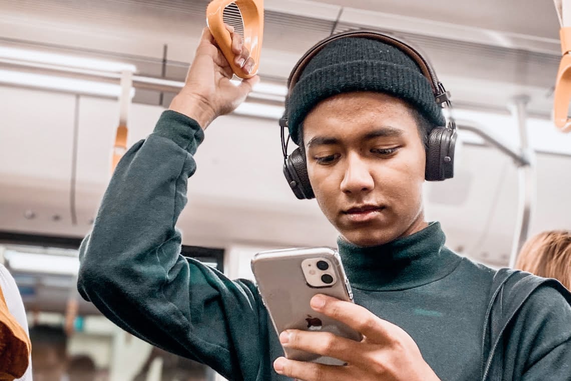 A man is standing in the underground with a mobile phone in his hand. He is looking at the singing exercises app.