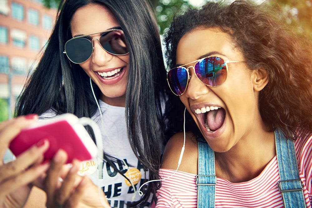 Two enthusiastic young women look at a mobile phone. They are using the Learn to Sing app.