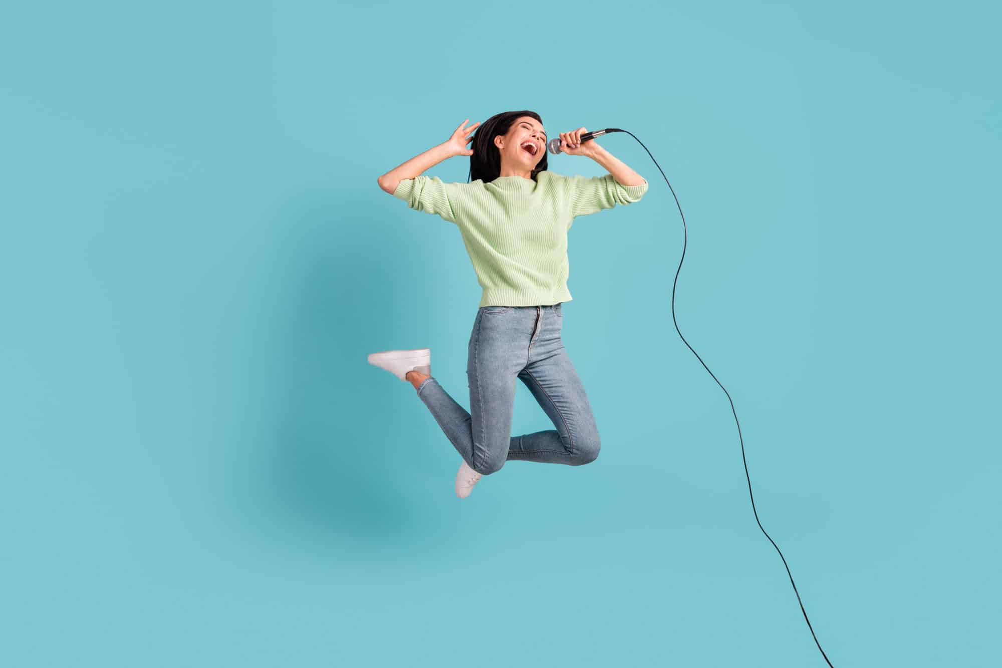 Eine Frau mit Mikrofon springt erfreut in die Höhe - das Bild steht symbolisch für das erfolgreiche Singen von vocal riffs and runs